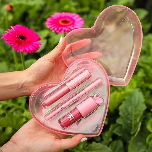 imagem de um estojo de um  kit gloss + lápis labial franciny ehlke com um fundo de plantas e flores de cor rosa pink ao fundo