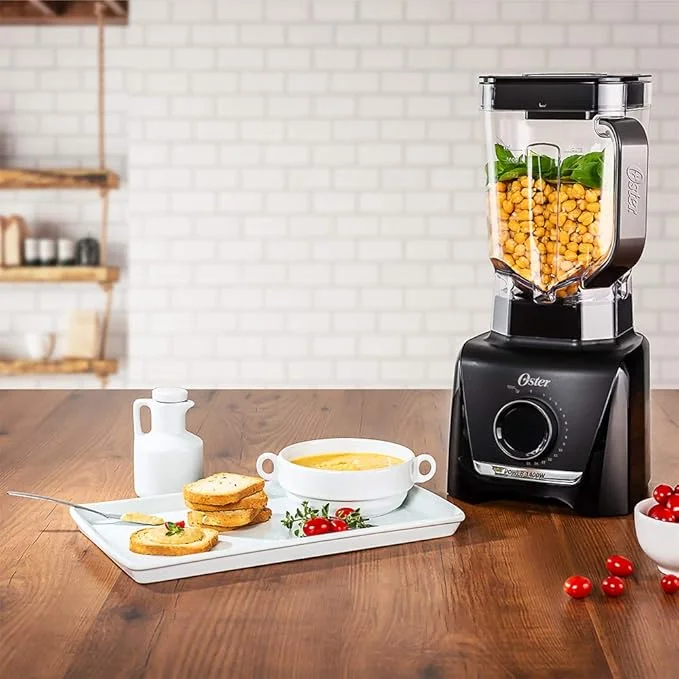 Liquidificador Oster 1400W Full Preto é bom? Vale a pena comprar na Amazon? Imagem de um liquidificador oster 1400 w full preto em cima de uma mesa de madeira dentro de uma cozinha